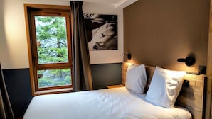 A neatly made bed with white linens, a large window with curtains, a wall-mounted artwork, and a bedside table with a lamp. - Cosy apartment in Courchevel 1550 (Courchevel)