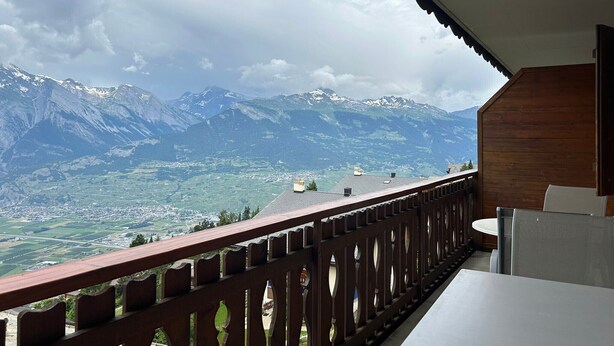 A balcony with a view of snow-capped mountains and a valley below.