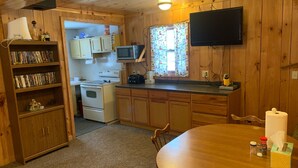 A cozy kitchen with wooden cabinets, a microwave, a stove, and a dining table with chairs. - 5 bedroom home in Paradise!!  4 miles from Tahquamenon Falls (Paradise)
