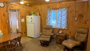 A cozy room with a wooden interior, a dining table with chairs, a refrigerator, two leather recliners, and a window with patterned curtains. - 5 bedroom home in Paradise!!  4 miles from Tahquamenon Falls (Paradise)
