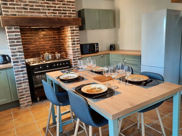 A kitchen with a brick wall, a stove, and a dining table set with plates and glasses. - La Jouvencière, rated 3 *** (Jouy)