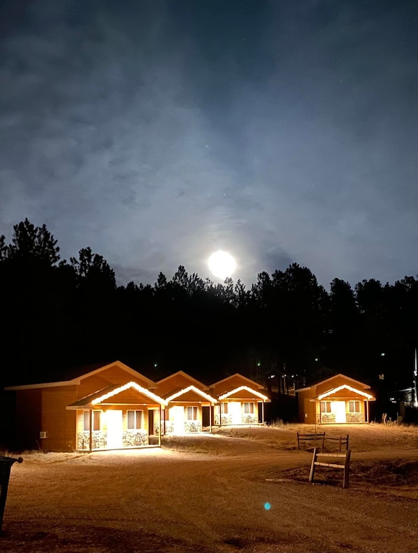 A row of three cabins with a large moon in the sky.