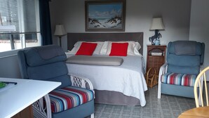 A hotel room with a bed, two chairs, a table, and a painting on the wall. - A private waterfront Lake Ida setting located in the middle of 23 acres (Boynton Beach)