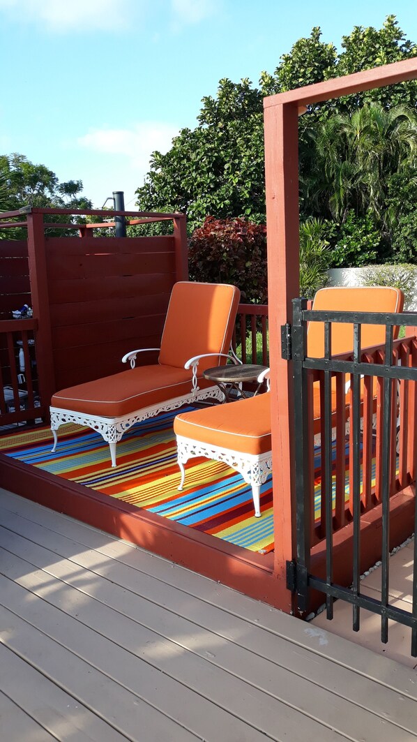 A deck with two orange lounge chairs, a small table, and a colorful striped rug.