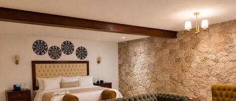 A hotel room with a bed, a green sofa, a yellow armchair, a stone wall, and a chandelier.