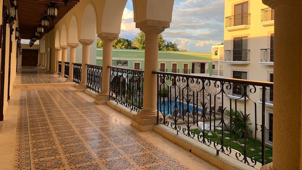 A covered corridor with patterned floor tiles, arches, and a balcony with a pool view. - Real Hispano (Valladolid)