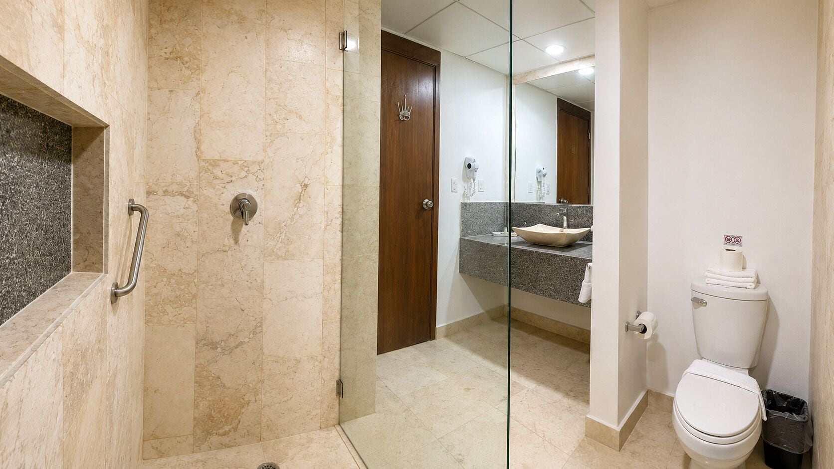 Un baño con cabina de ducha de vidrio, inodoro y tocador con lavamanos.