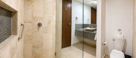 Un baño con cabina de ducha de vidrio, inodoro y tocador con lavamanos.