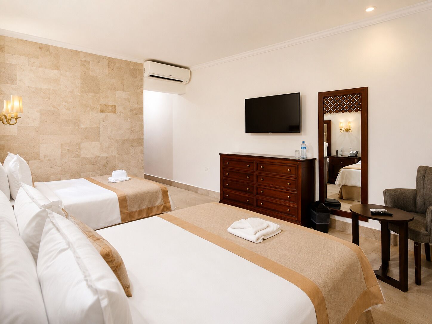 A hotel room with two beds, a TV, a dresser, a chair, and a mirror.