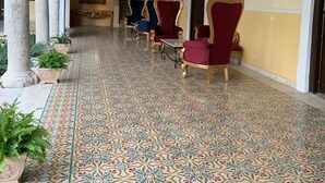 A corridor with ornate chairs and a patterned floor, leading to a staircase. - Real Hispano (Valladolid)