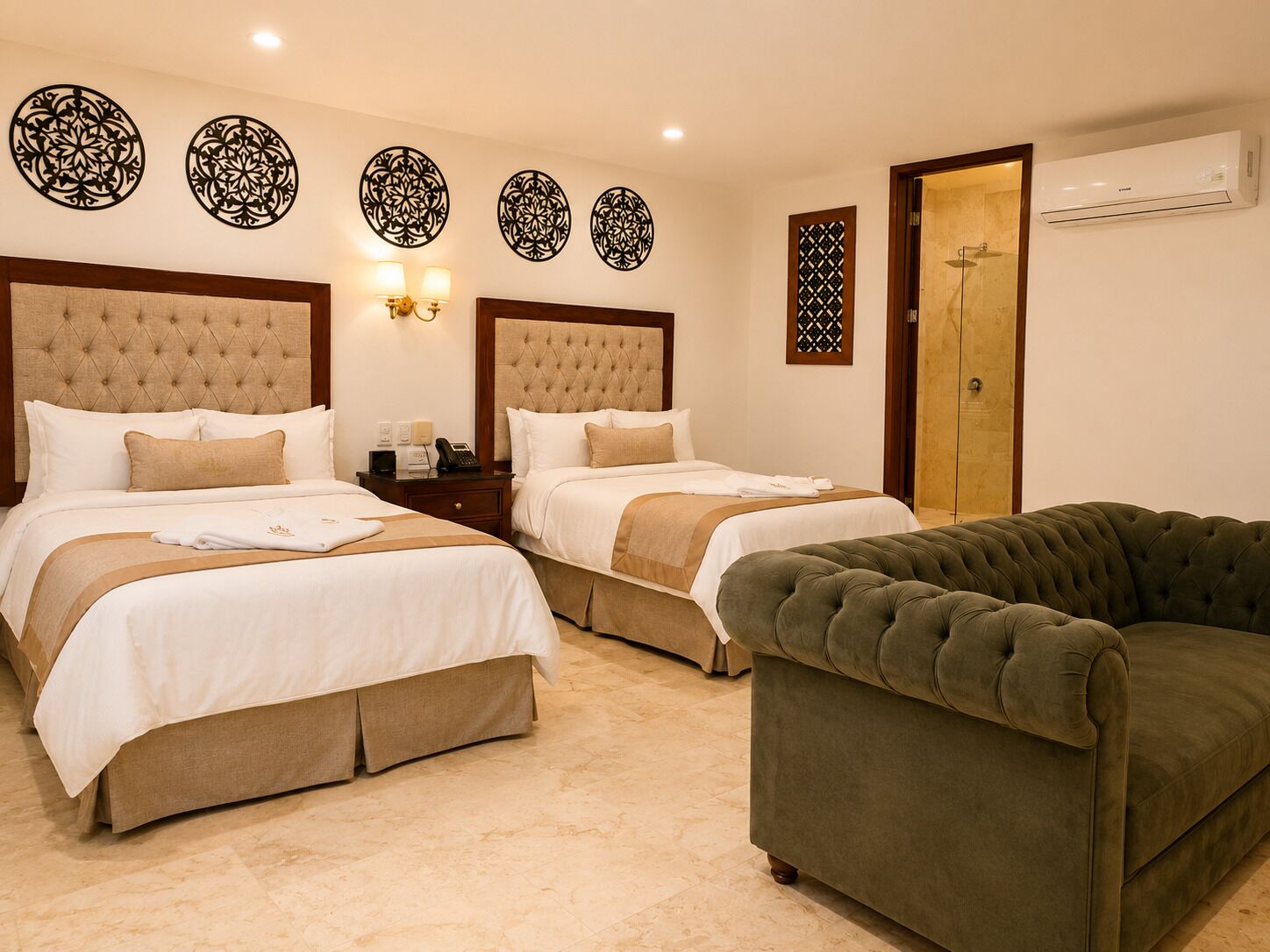 A hotel room with two beds, a green sofa, decorative wall art, and an air conditioning unit.