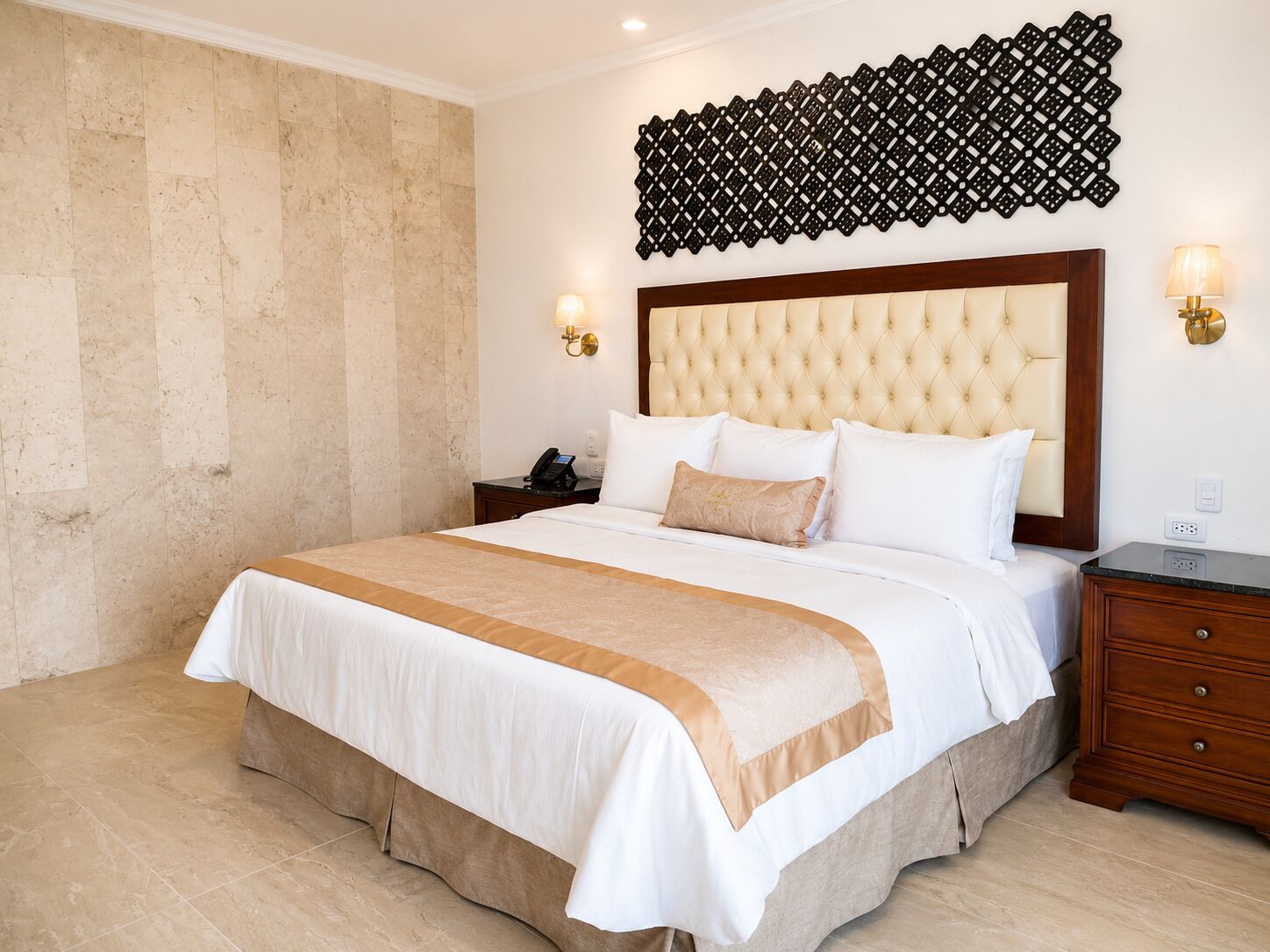 Una camera d'albergo con un letto grande, una testiera, lampade sui comodini, un tavolino e un pannello decorativo a parete.