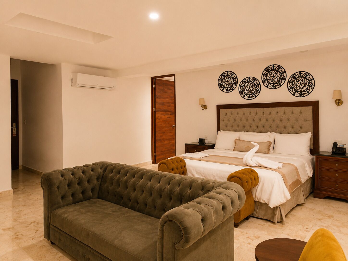 A hotel room with a bed, a sofa, a bedside table, and decorative wall art.