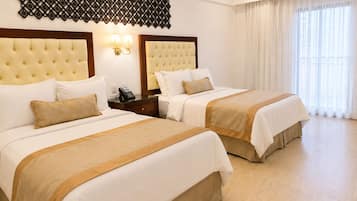 Une chambre d’hôtel avec deux lits, un luminaire fixé au mur et une grande fenêtre avec des rideaux.