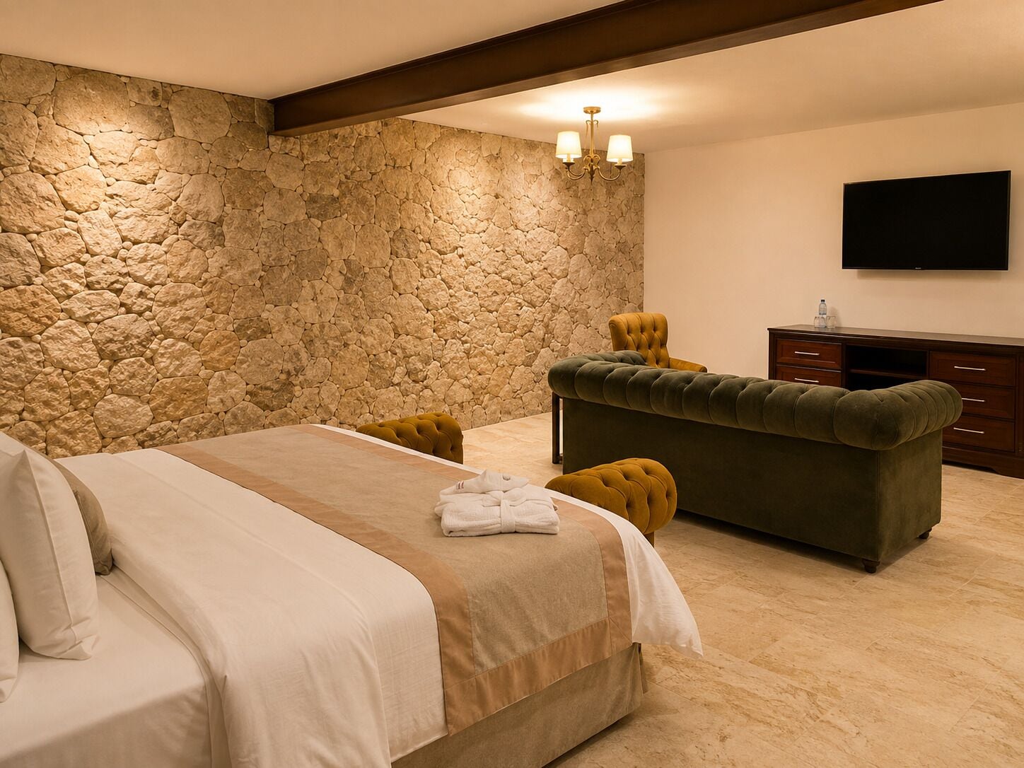 Un dormitorio con pared de piedra, cama con cubrecama beige y marrón, sofá verde y televisor de pantalla plana en la pared.