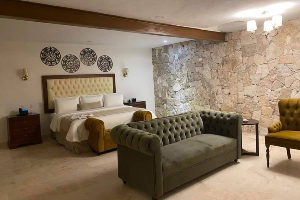 A bedroom with a bed, a green sofa, a yellow armchair, and a stone wall.