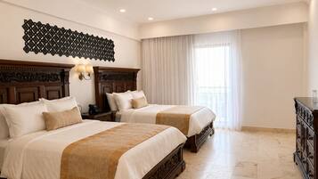 Habitación de hotel con dos camas, cabecero de madera, mesita de noche con lámpara, ventana grande con cortinas y cómoda.