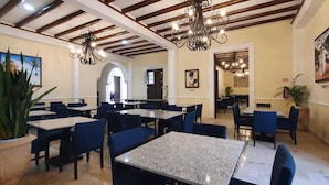 A restaurant with multiple tables and chairs, chandeliers, and framed artwork on the walls. - Real Hispano (Valladolid)