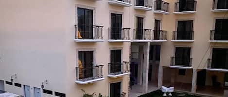 A multi-story building with balconies, a swimming pool, and a small garden area with a fountain.