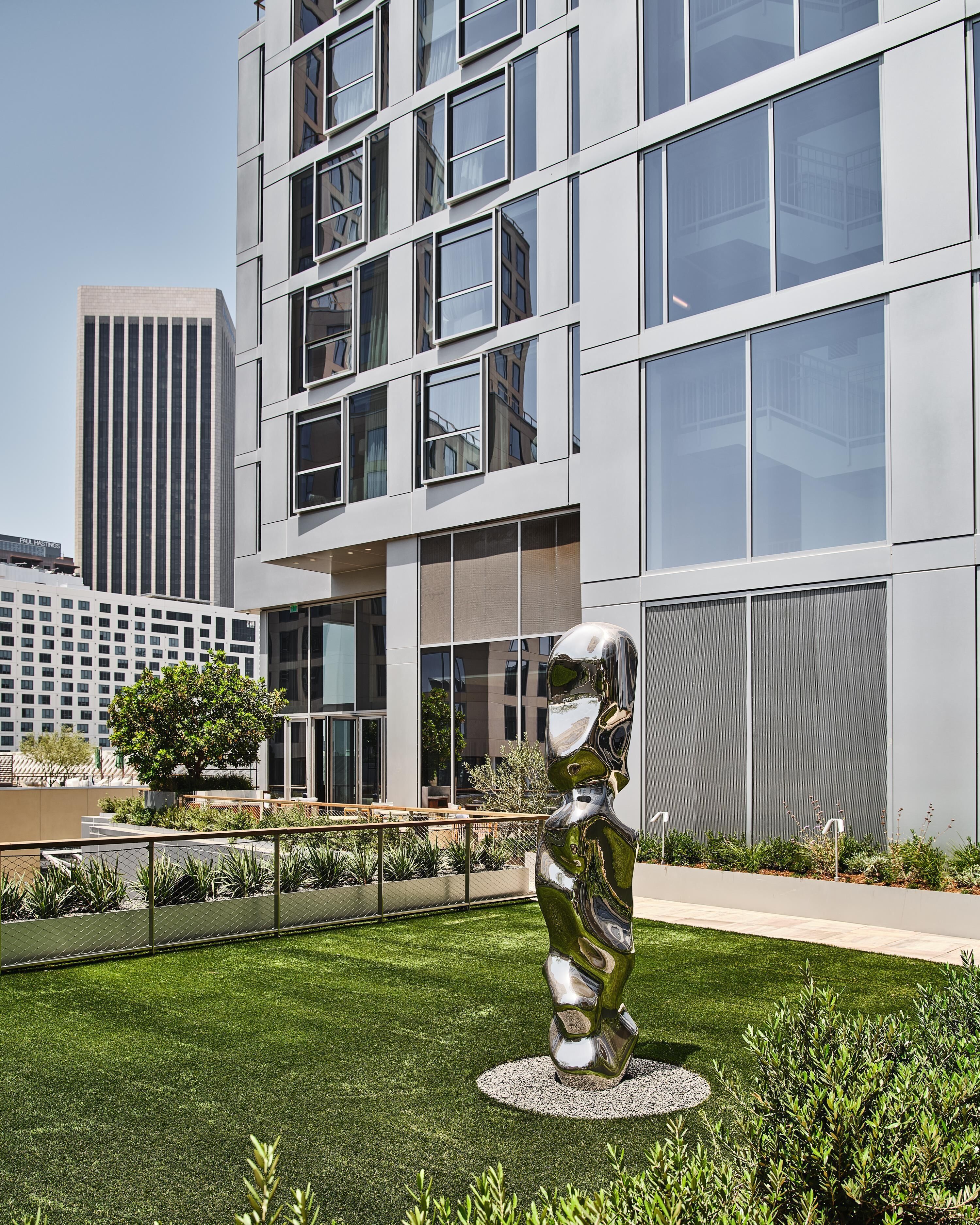 A modern building with a glass facade, a sculpture in the foreground, and a well-maintained lawn.