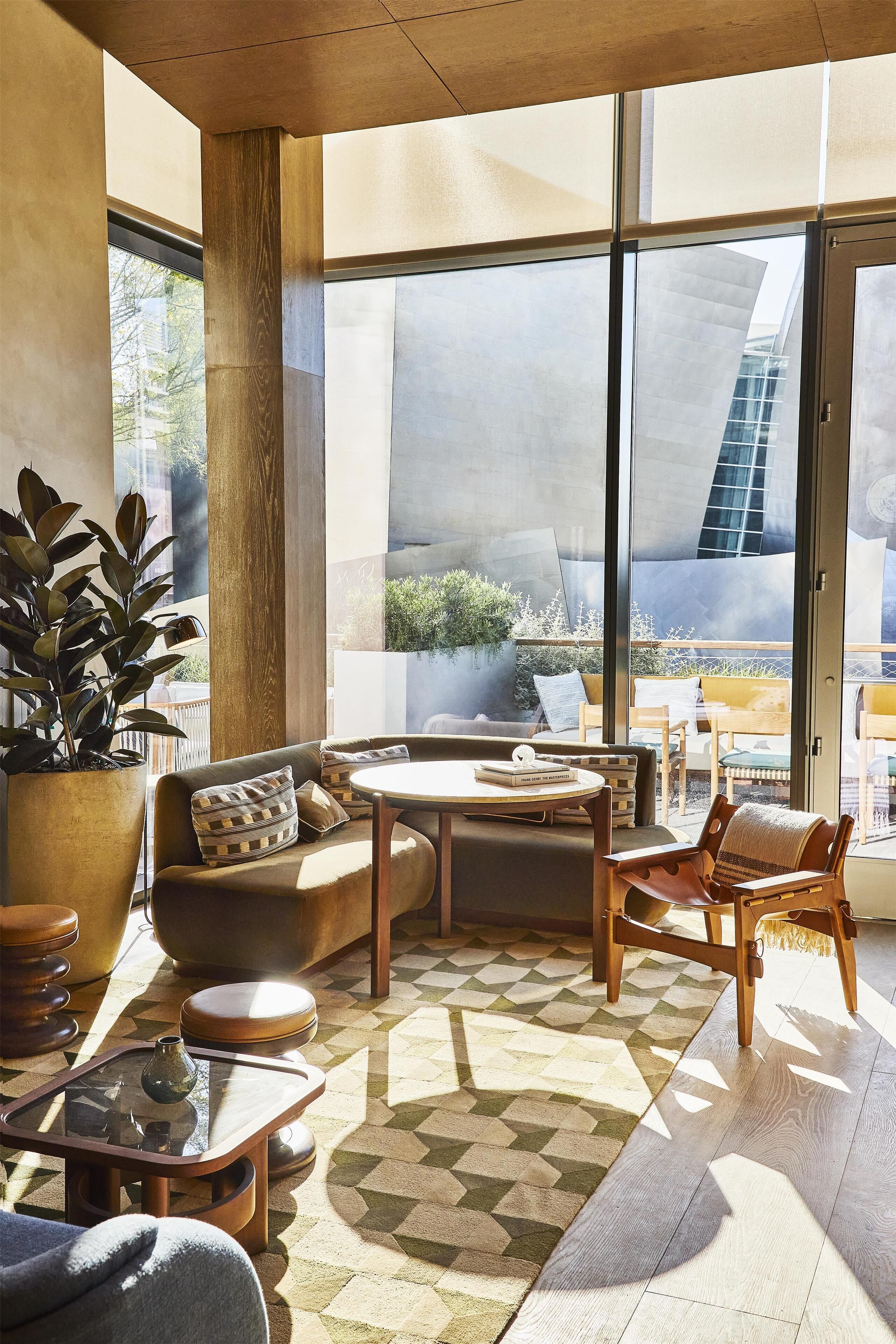 A modern living room with a large window, a sofa, a coffee table, and a potted plant.