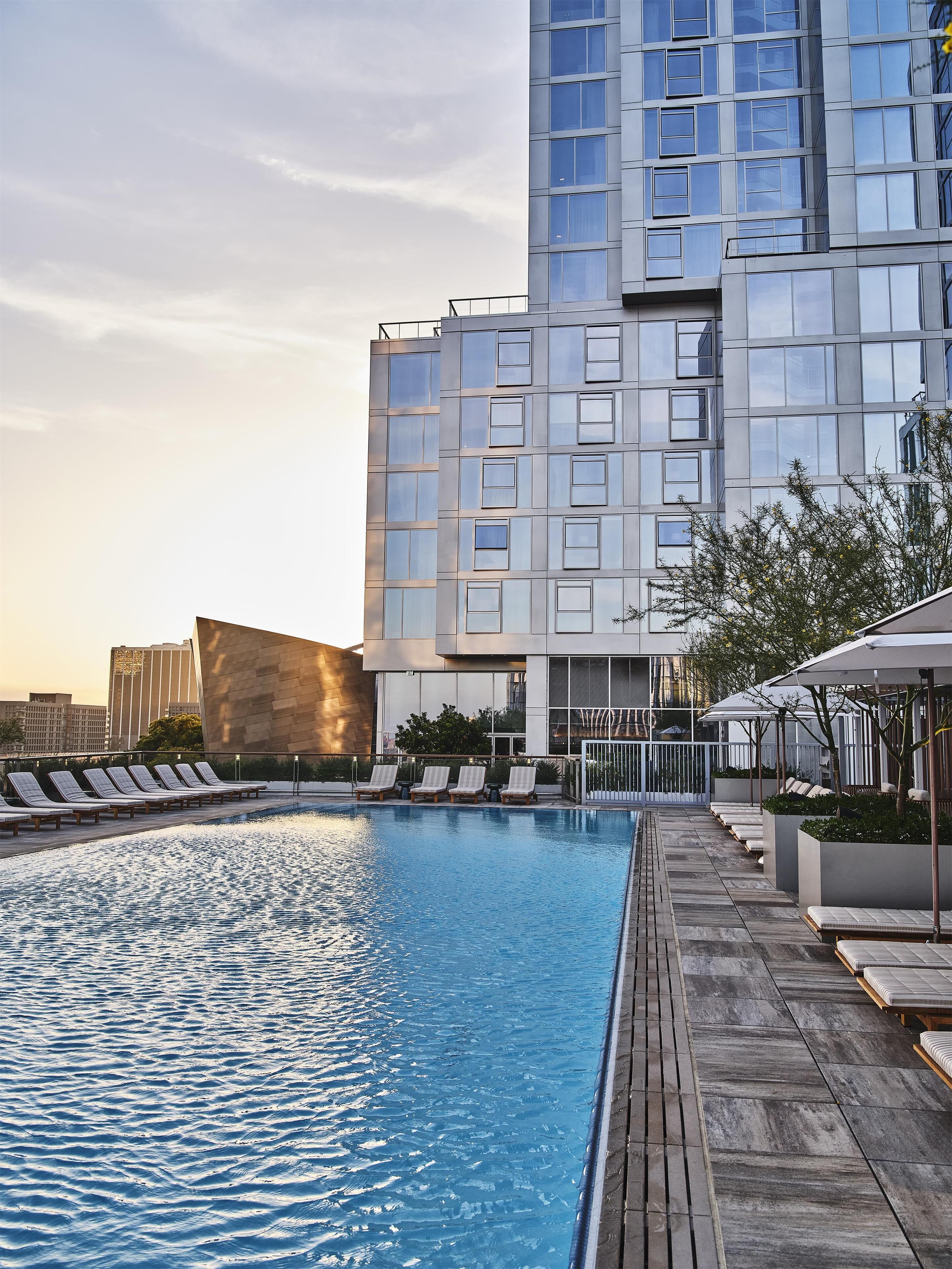 Un hotel moderno con piscina en la azotea, sillones de descanso y vistas al horizonte de la ciudad.