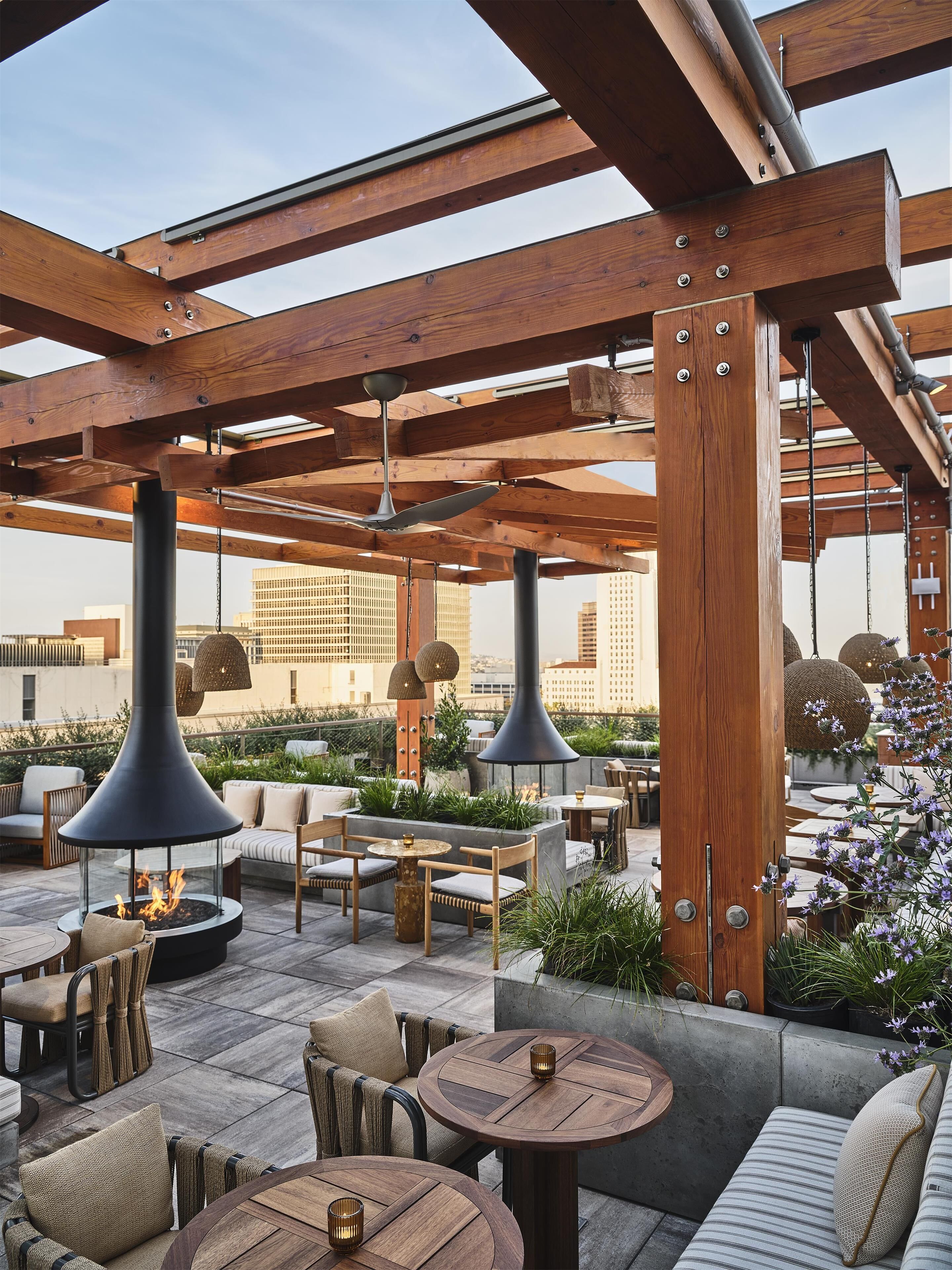 An outdoor seating area with wooden beams, round tables, and hanging lamps.