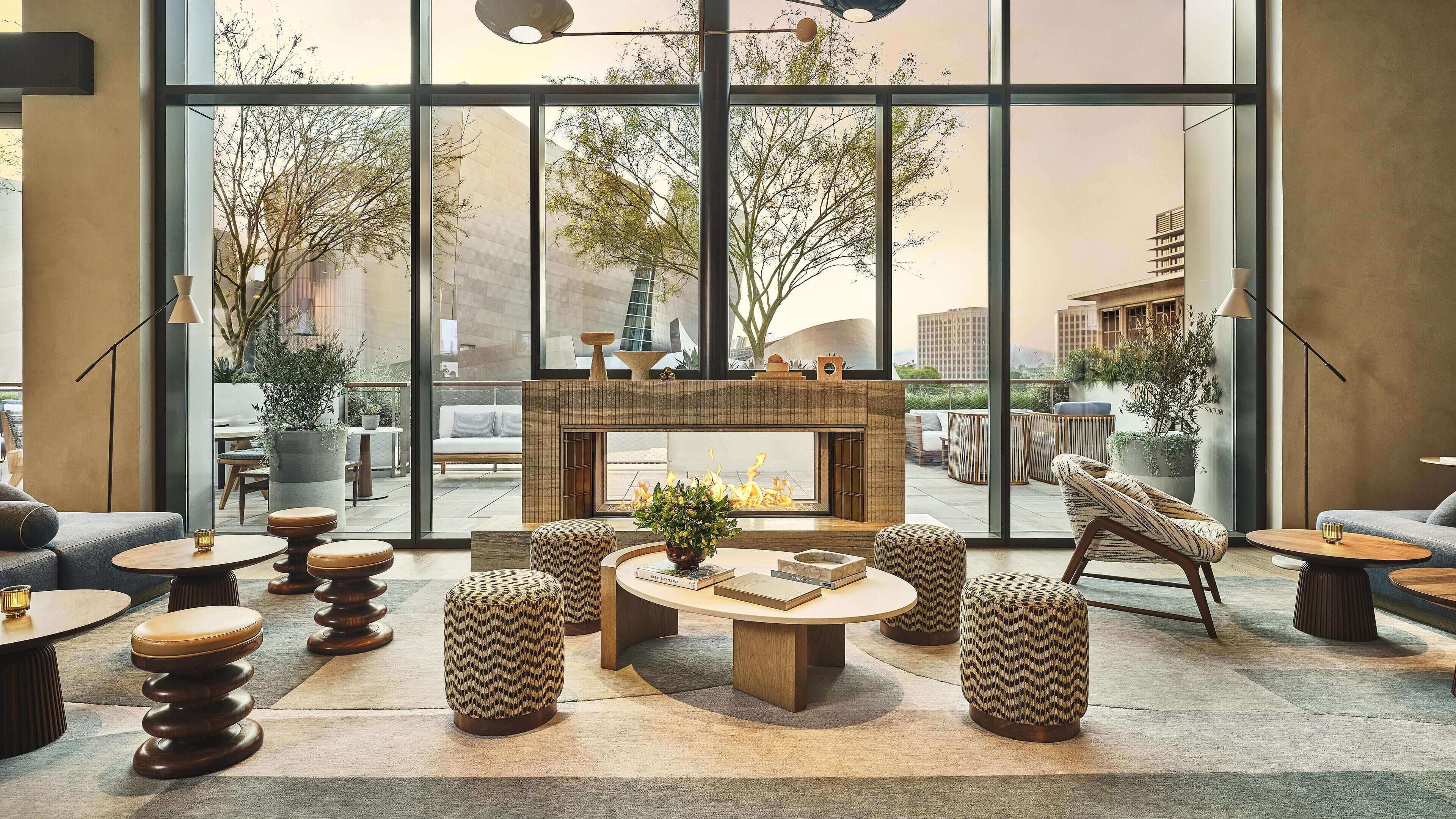 A modern lounge area with a fireplace, seating, and large windows offering a view of the cityscape.