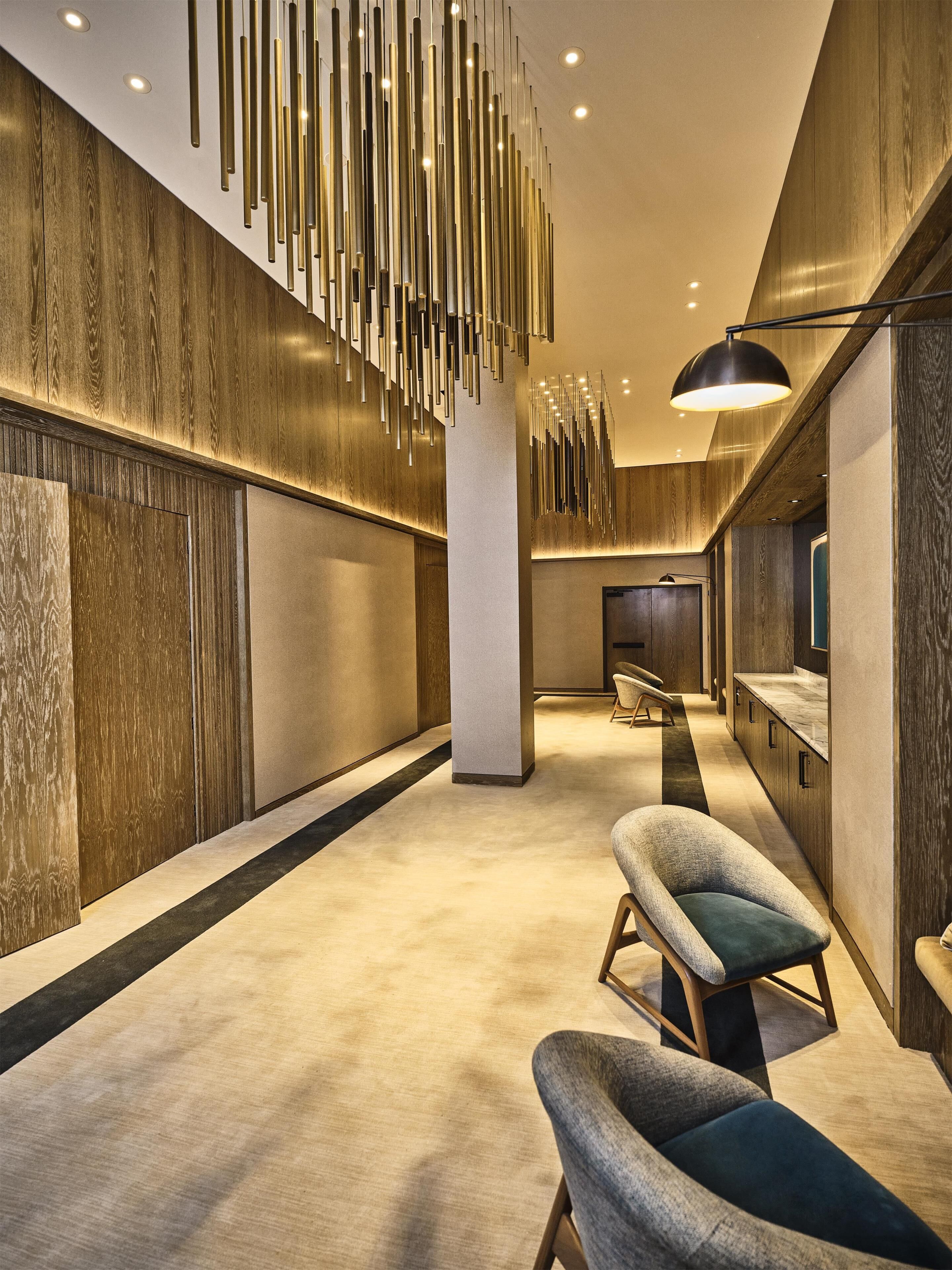 Un interior moderno con un largo pasillo, paredes de paneles de madera, una columna central y una zona de estar con un banco y una silla.