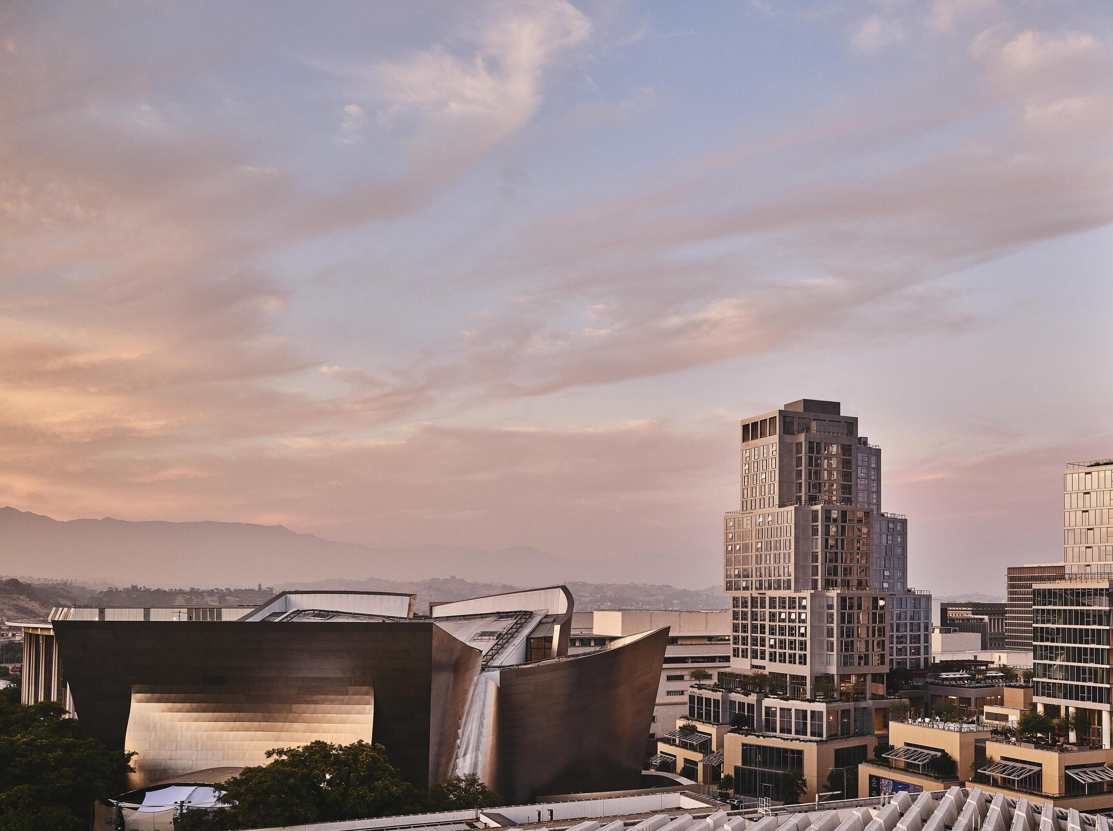 A modern urban landscape with a prominent building featuring a unique, angular design and a waterfall feature.