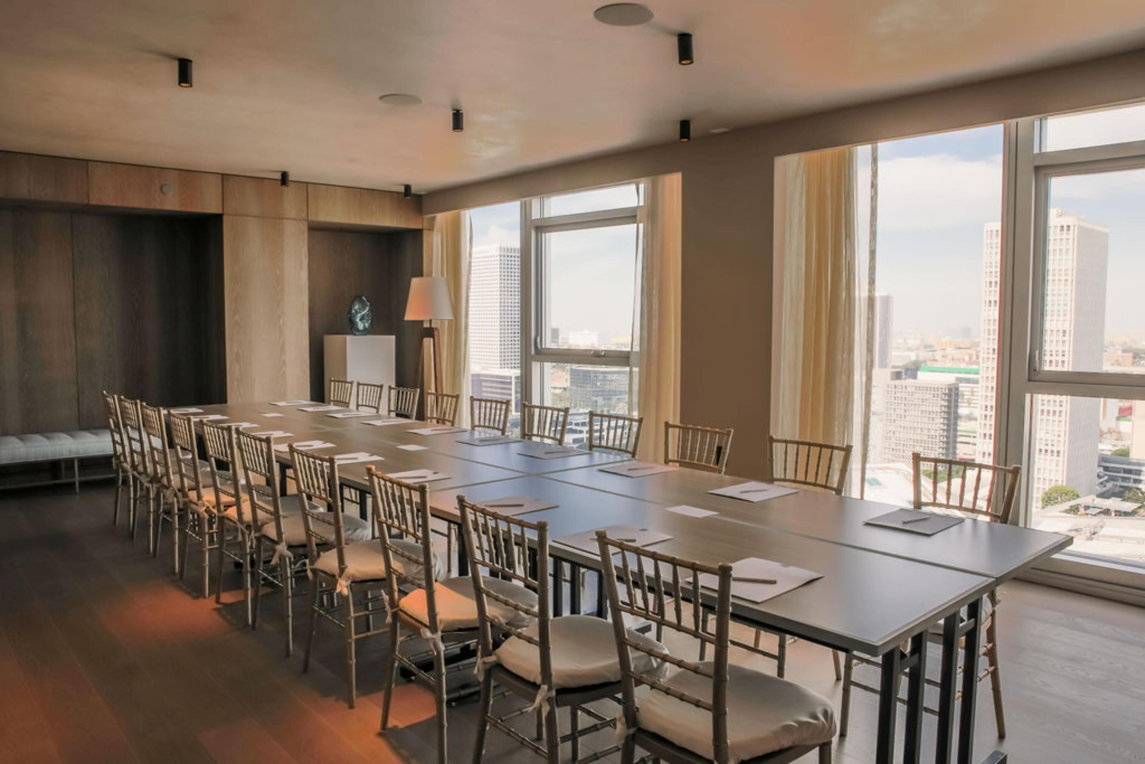 A conference room with a long table and chairs, large windows with city views, and a modern design.