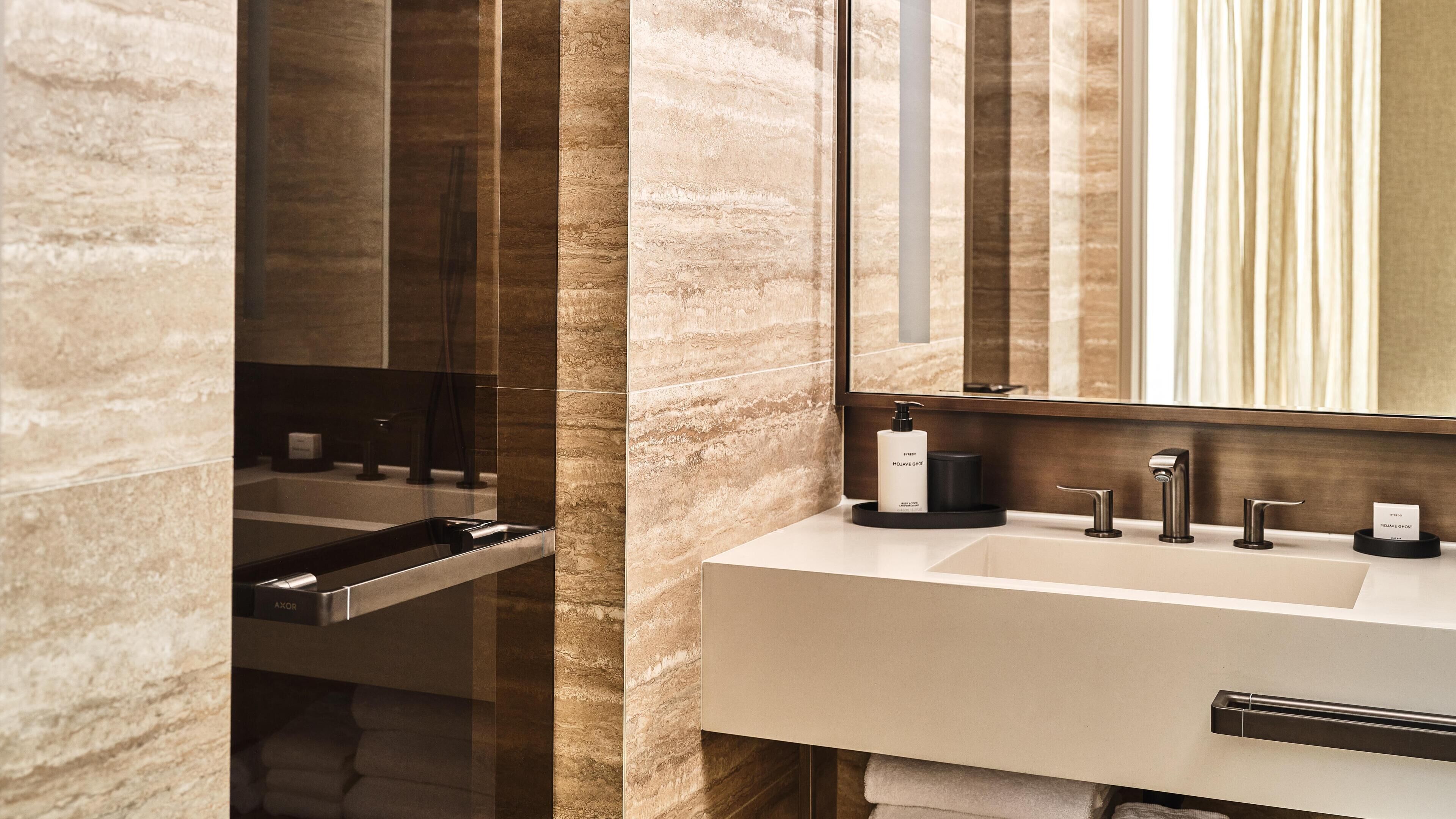 A modern bathroom with a large mirror, a white sink, and a black faucet.