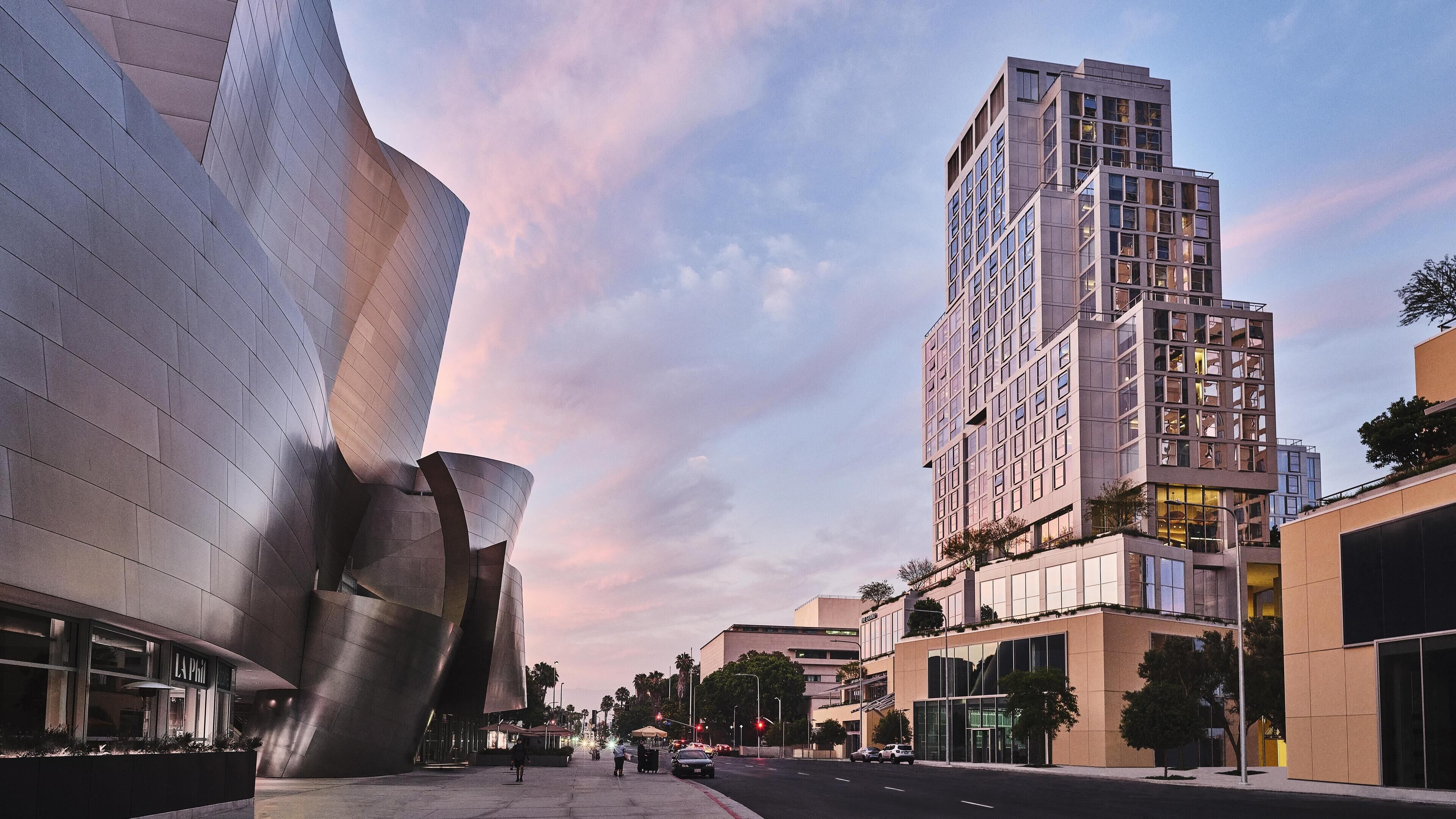 A modern building with a unique curved facade and a tall adjacent structure with a grid-like window pattern.