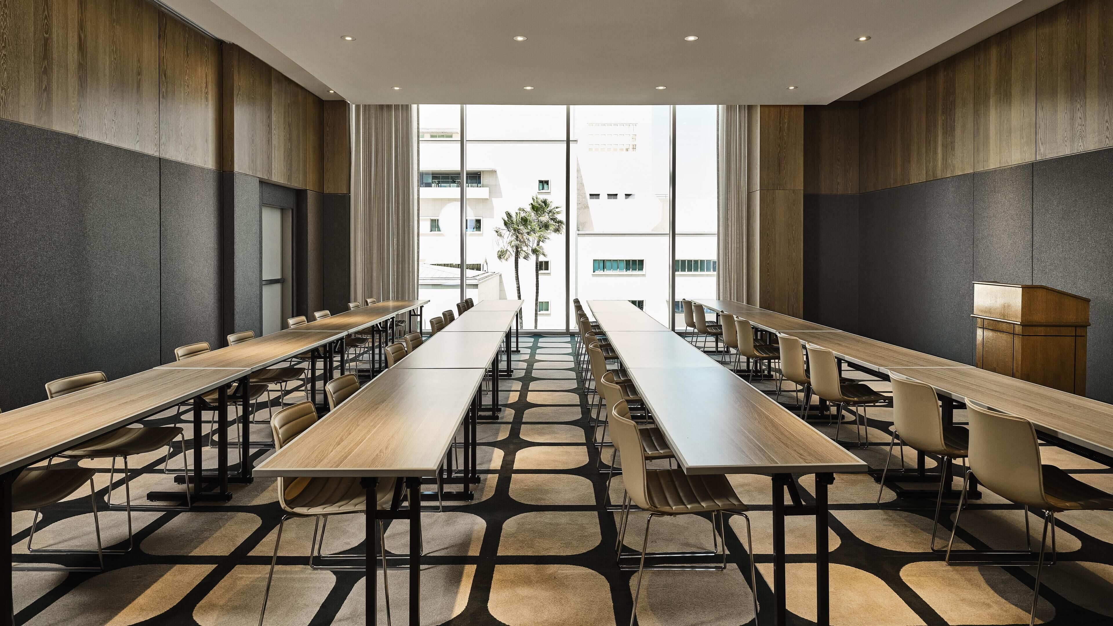 Een vergaderruimte met lange tafels en stoelen, grote ramen en een modern design.
