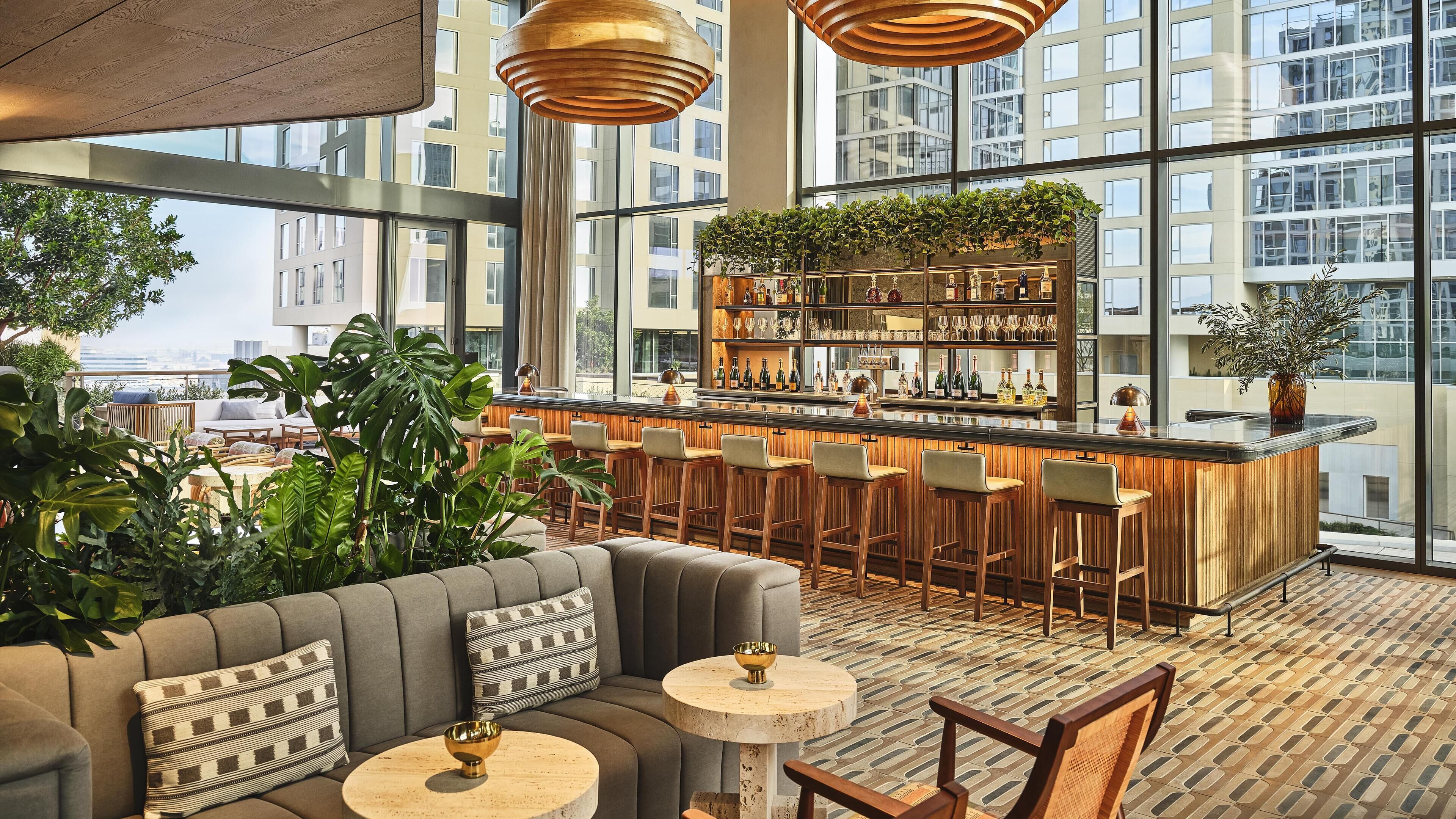 A modern bar area with a wooden bar counter, bar stools, and a seating area with a sofa and round tables.