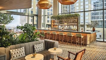 Un espace bar moderne avec un comptoir en bois, des tabourets de bar et un coin salon comprenant un canapé et des tables rondes.