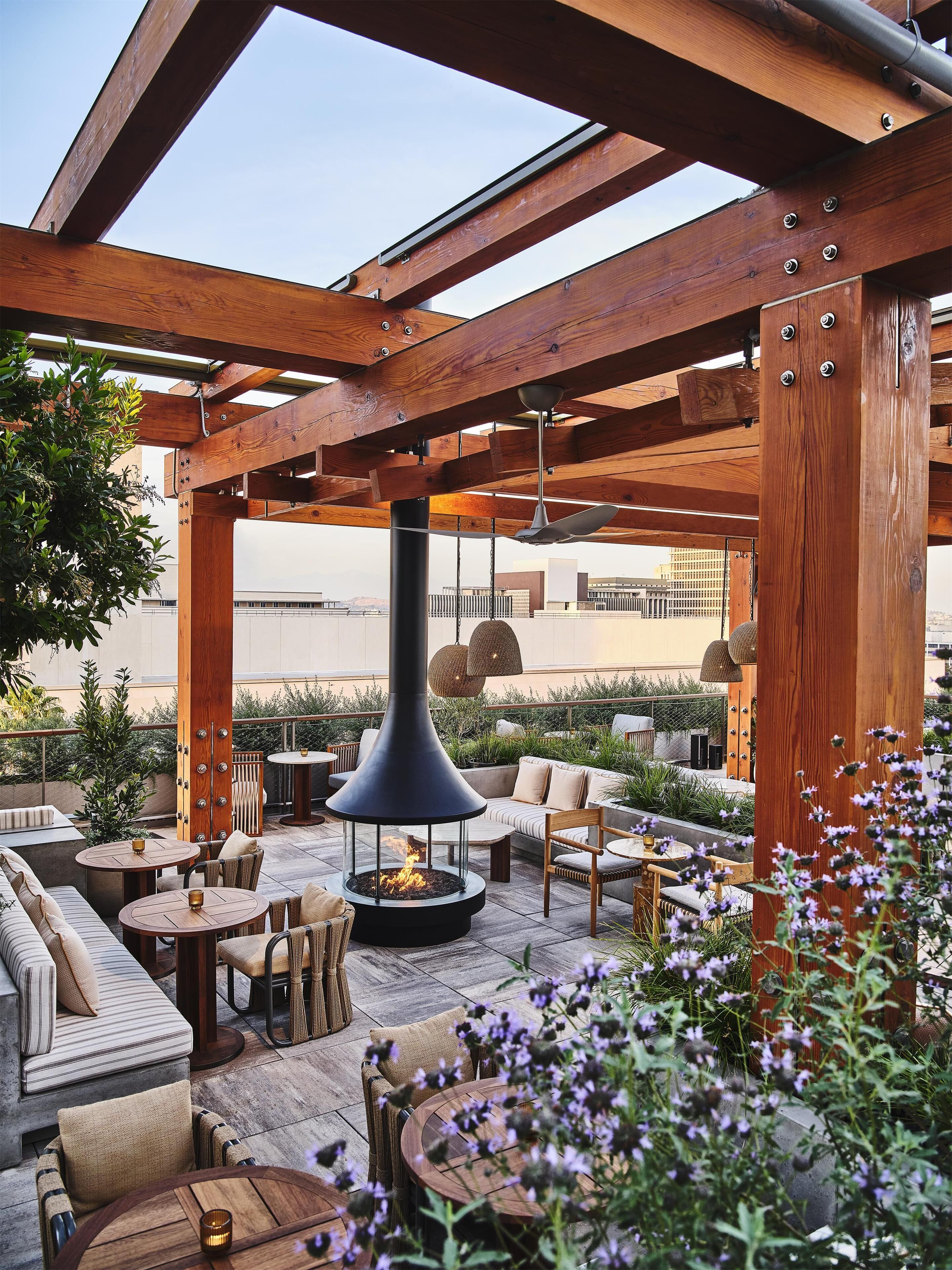An outdoor patio with wooden beams, round tables, and a central fire feature.