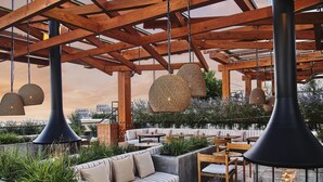 An outdoor seating area with a fire pit, wooden beams, and hanging wicker lamps. - Conrad Los Angeles (Los Angeles)