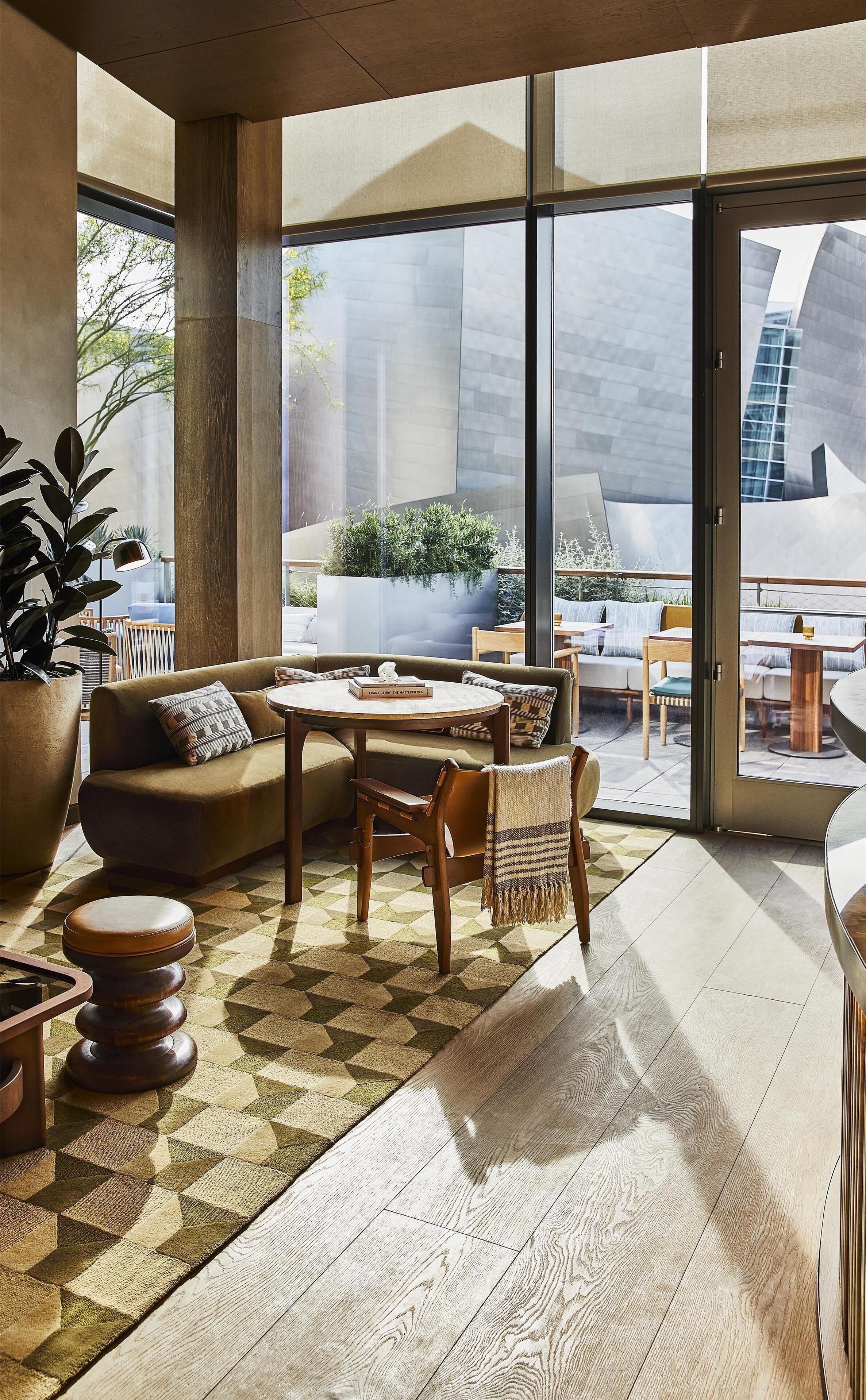 A modern interior with a large window, a sofa, a table, and a potted plant.