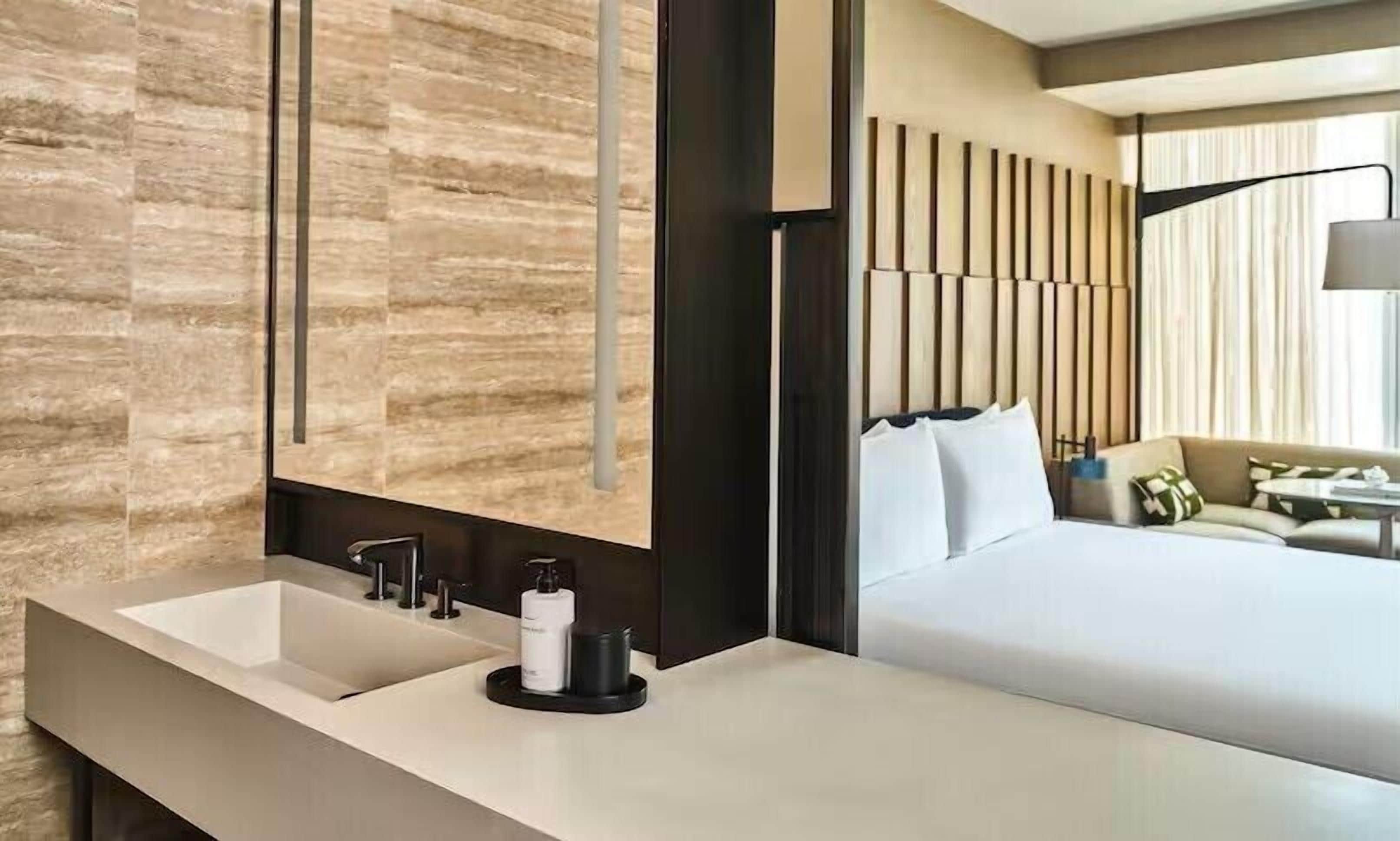 Una habitación de hotel moderna con una cama grande, un lavamanos doble y un espejo amplio.