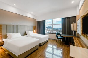 Ein Hotelzimmer mit zwei Betten, einem Schreibtisch, einem Stuhl und einem großen Fenster mit Blick auf die Stadt.