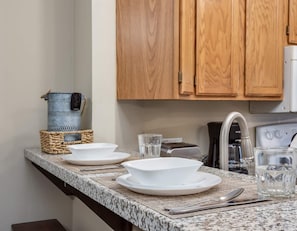 Kitchen area with granite countertop, featuring a coffee maker, plates, glass, and utensils.