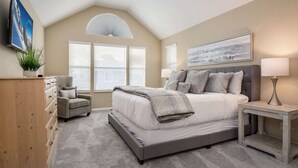 A bedroom with a large bed, a nightstand, a dresser, and a chair.