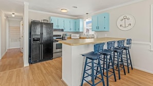 A kitchen with light blue cabinets, a black refrigerator, a wooden island with blue bar stools, and a white wall with a decorative anchor. - 4BR 3 Bath, Dog Friendly, Linens & Towels provided, 700ft to beach access (Kill Devil Hills)