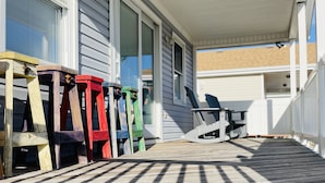 A covered porch with a wooden deck, a row of colorful chairs, and a table. - 4BR 3 Bath, Dog Friendly, Linens & Towels provided, 700ft to beach access (Kill Devil Hills)