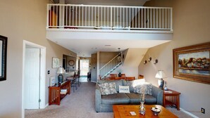 Ein geräumiges Wohnzimmer mit hohen Decken, einer Treppe zu einer oberen Ebene, einem Essbereich und einer gemütlichen Sitzecke mit Sofa und Couchtisch.