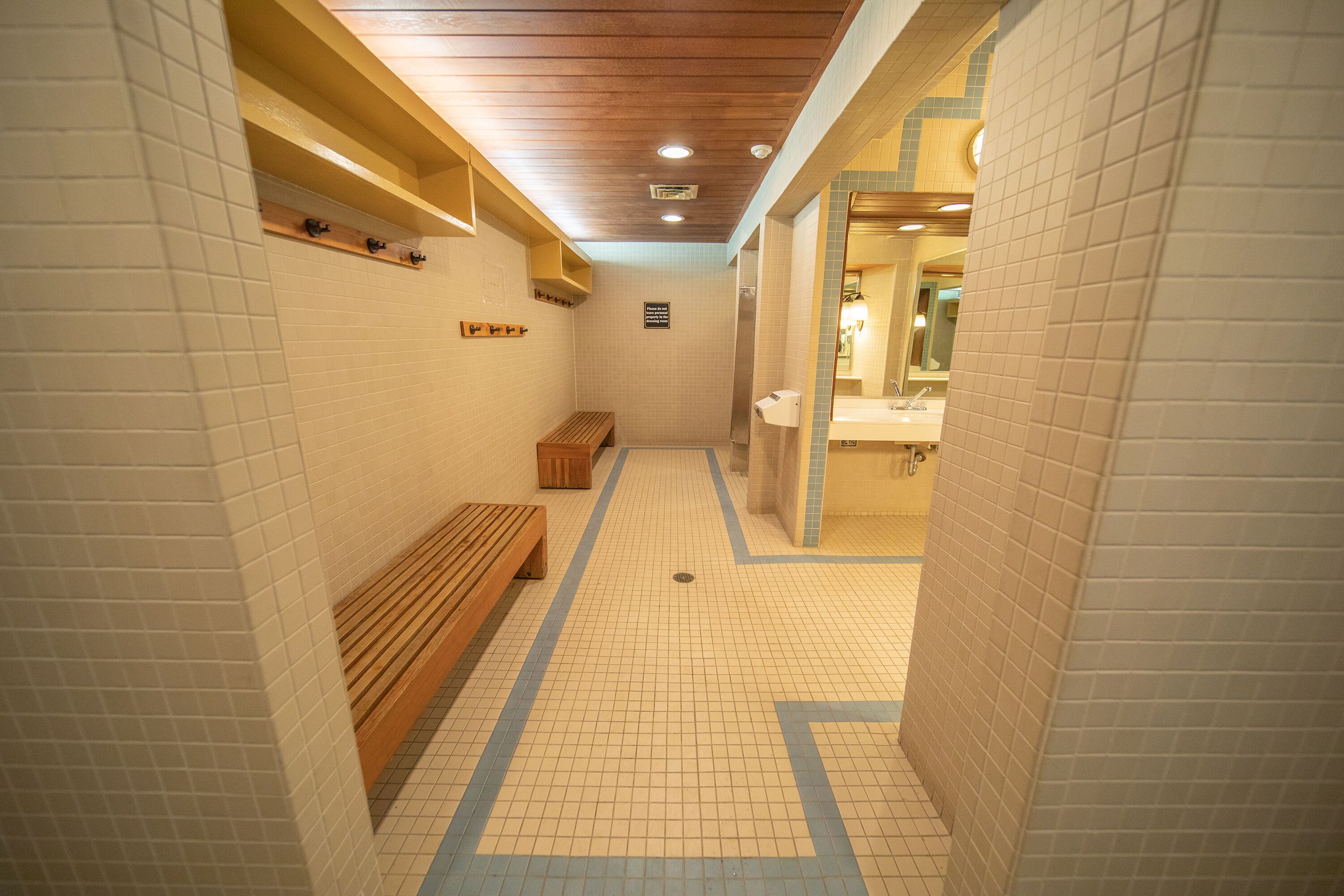 Ein gefliester Flur mit einer Bank, einem Holzregal und einem im Hintergrund sichtbaren WC.