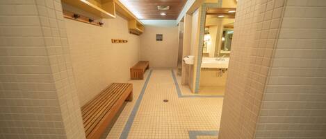 Ein gefliester Flur mit einer Bank, einem Holzregal und einem im Hintergrund sichtbaren WC.