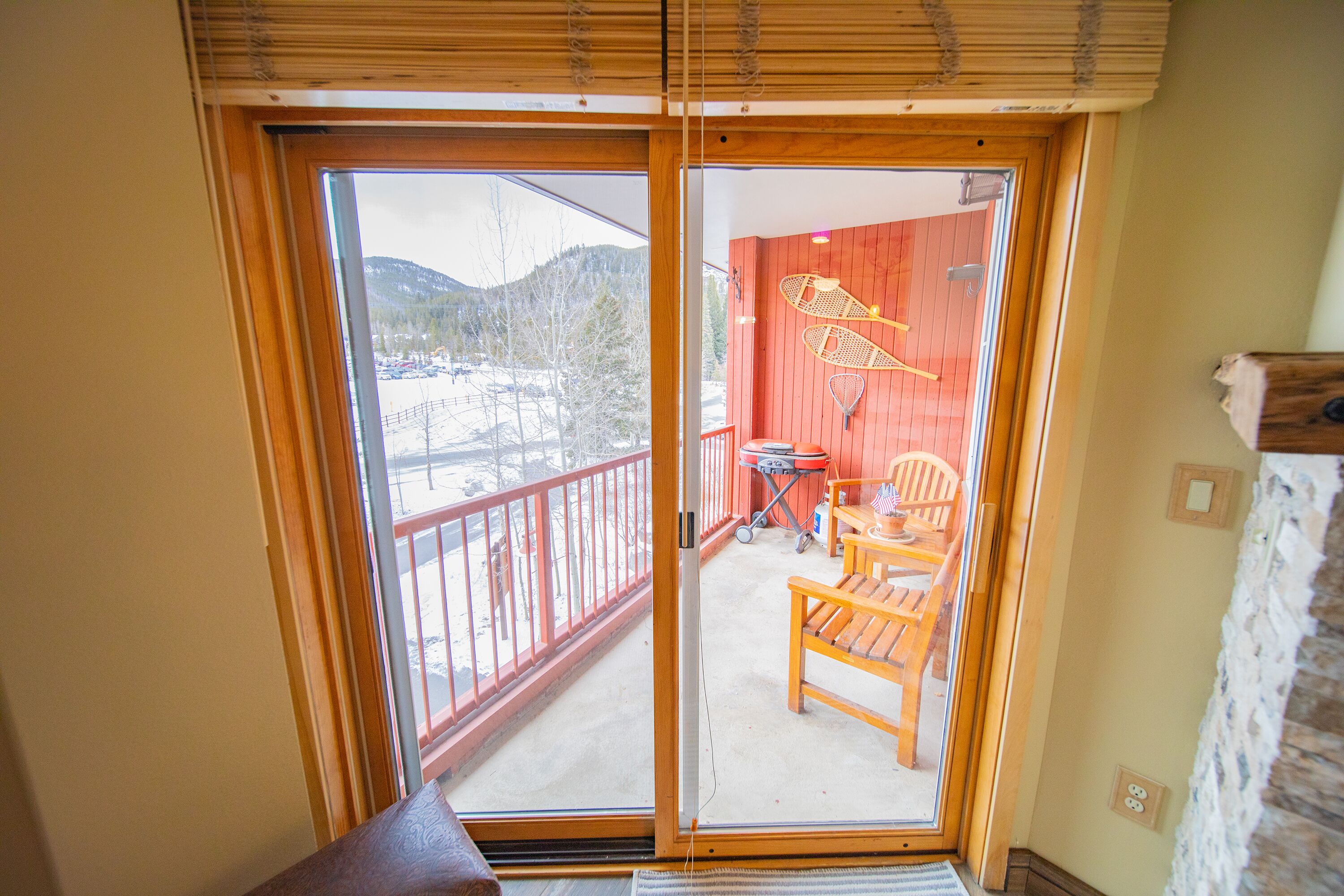 A room with a sliding glass door leading to an outdoor balcony with a red wall, a wooden chair, and a table.