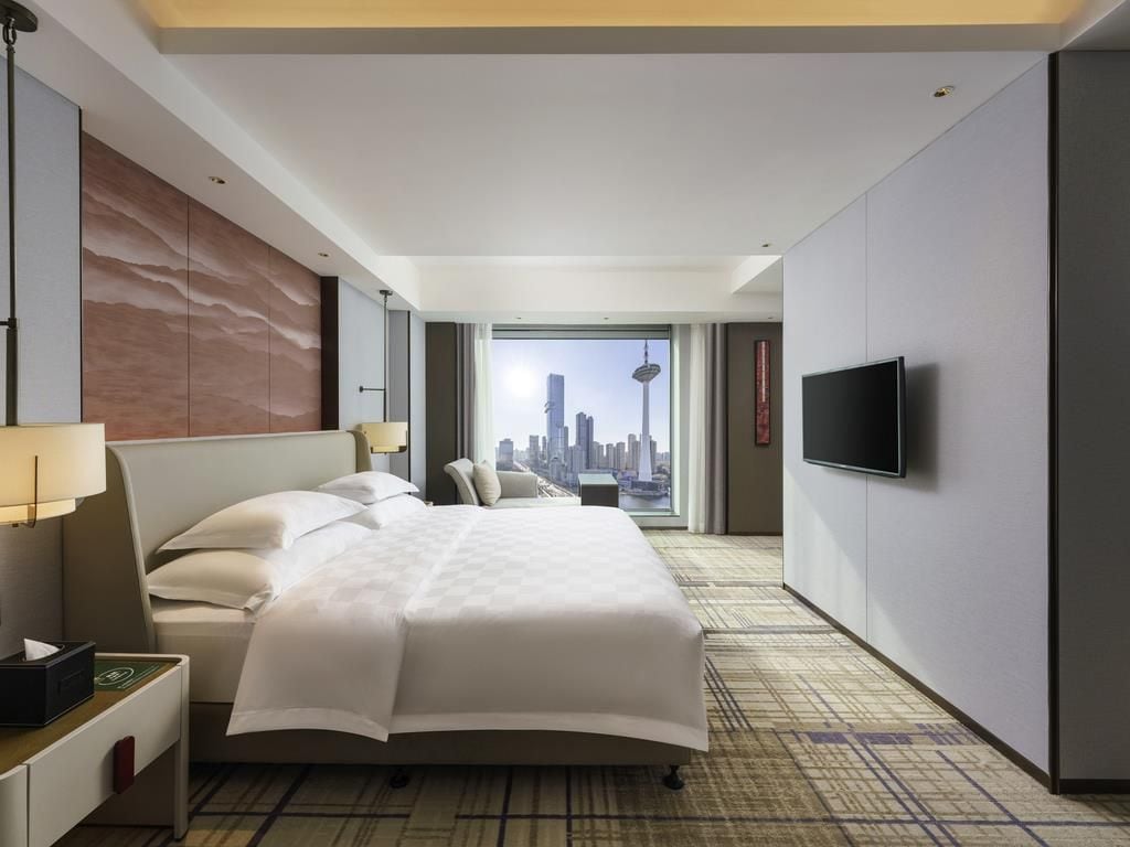 Una habitación de hotel con una cama grande, televisión y vistas a la ciudad.